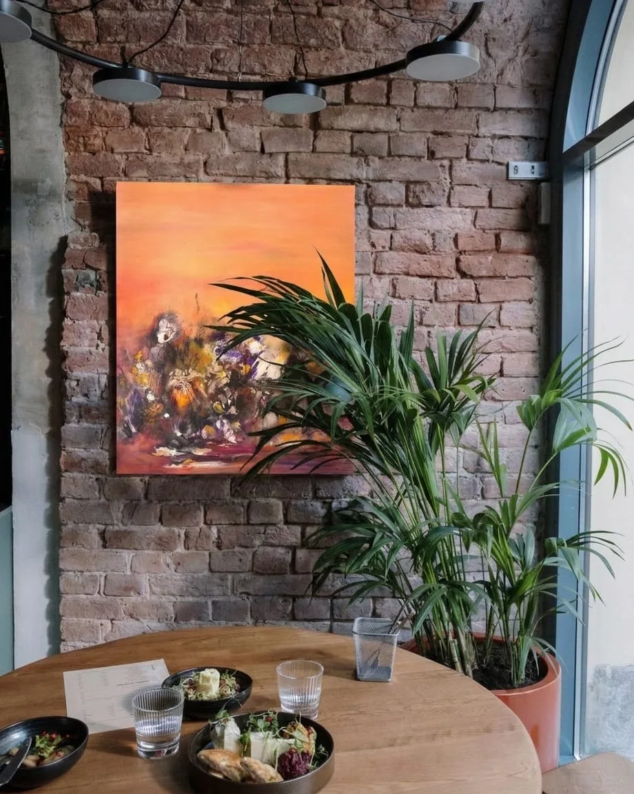 Beispielsituation: die abstrakte Leinwand Uluru von Régine Gardan an der Ziegelwand eines Café-Restaurants